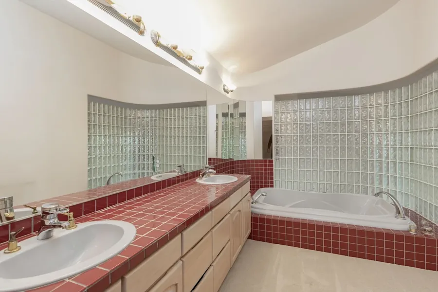 Original photo of a dated bathroom with red tile counters, a red tile tub surround and a light oak vanity