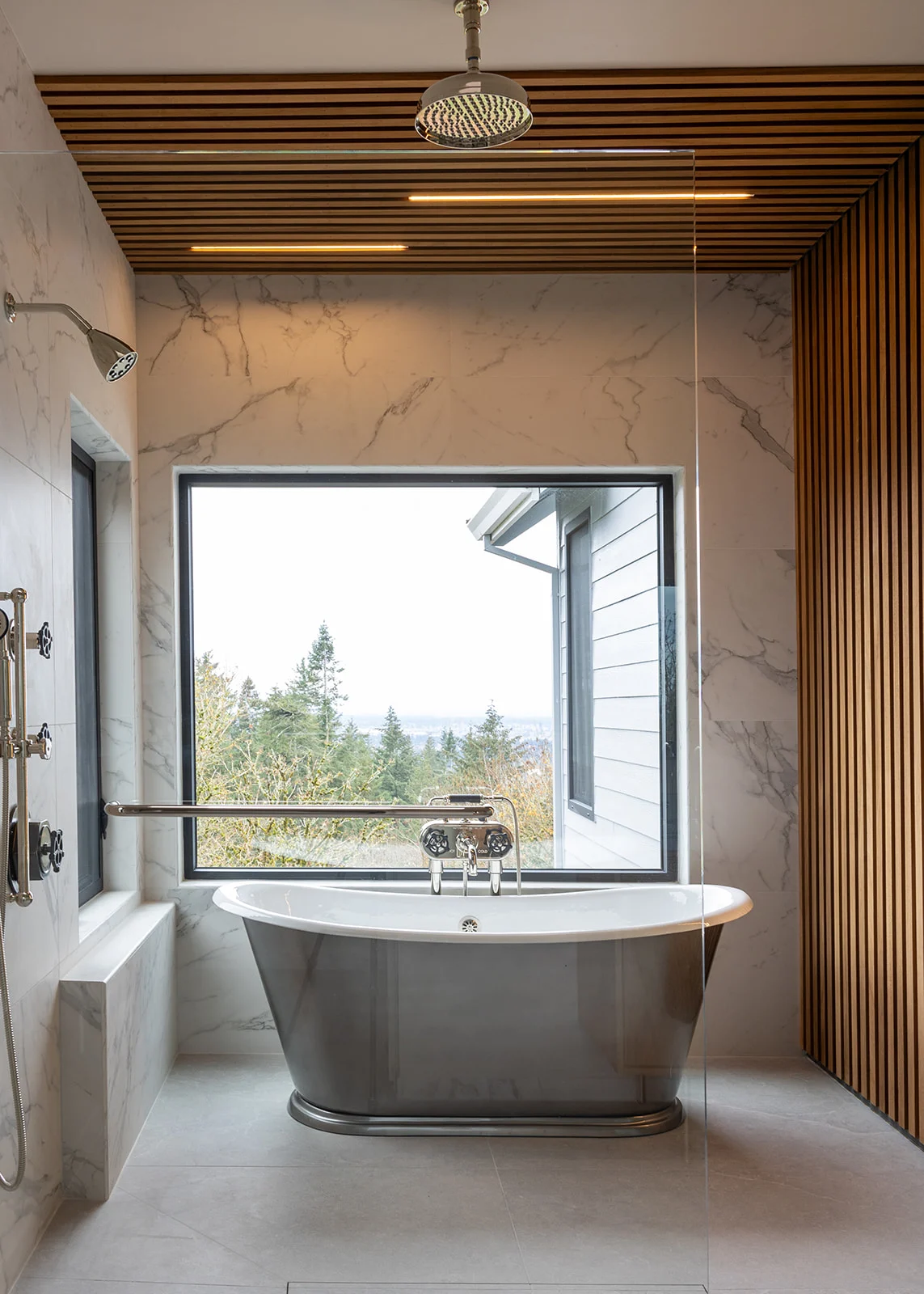 Primary bathroom with a freestanding tub under a picture window and wood slat accents, remodeled by JDI Construction